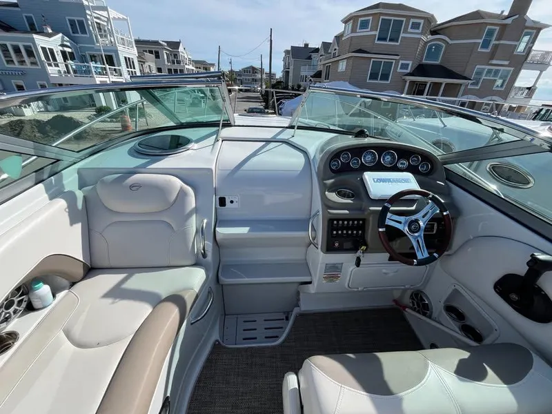 Slide: The Image of 2018 Crownline 264 CR boat interior with steering wheel, dashboard, and seating, docked near waterfront homes. - 27