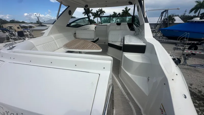 Slide: The Image of 2023 Sea Ray Sundancer 320 Outboard interior with white seating and wooden table, docked outdoors. - 3