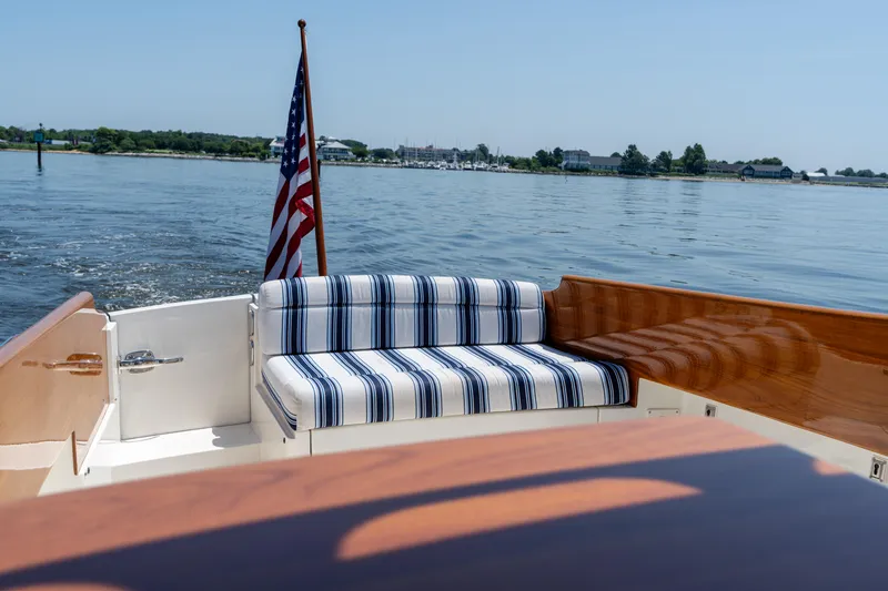 Slide: The Image of 2015 Hinckley Picnic Boat 37 MKIII with striped seating and American flag on calm water. - 18