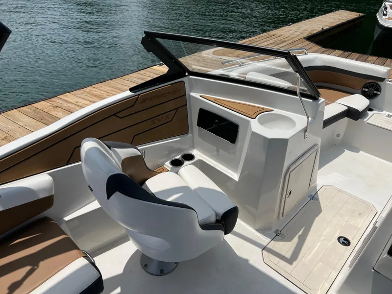 Slide: The Image of 2024 Starcraft SVX 210 IO boat interior with seating and console, docked by the water. - 11