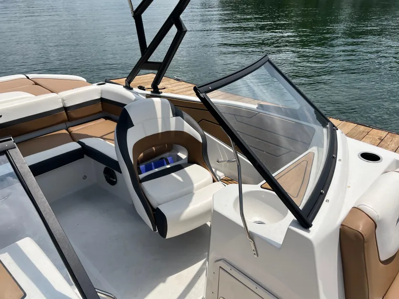 Slide: The Image of 2024 Starcraft SVX 210 IO boat interior with seating and windshield, docked on calm water. - 6