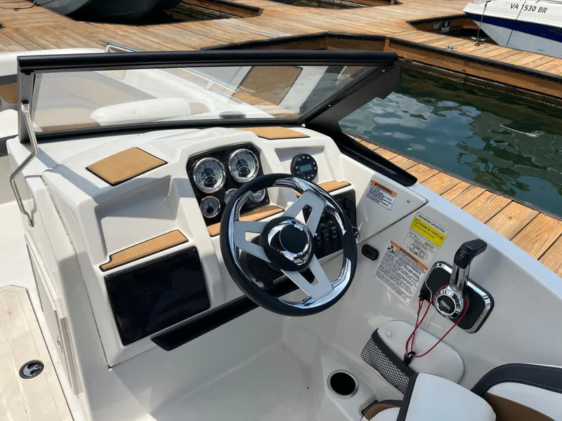 Slide: The Image of 2024 Starcraft SVX 210 IO boat dashboard with steering wheel and controls at a dock. - 9