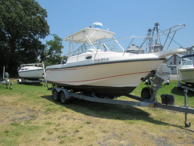 Slide: The Image of 1997 Boston Whaler 23 Conquest boat on trailer, parked on grass under clear sky. - 2
