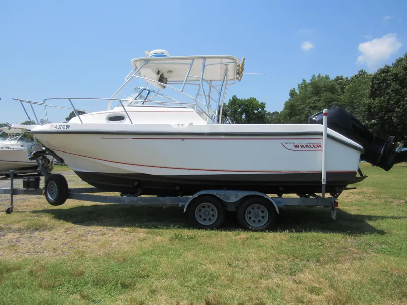 Slide: The Image of 1997 Boston Whaler 23 Conquest boat on trailer, parked on grass under clear sky. - 5