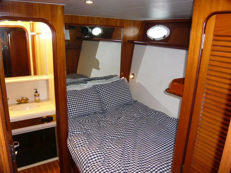 Slide: The Image of 1990 Viking Cockpit Motor Yacht cabin with bed, checkered bedding, and compact bathroom. - 25