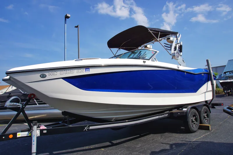 The Image of 2019 MasterCraft X24 boat on trailer, blue and white design, under clear sky. - 0