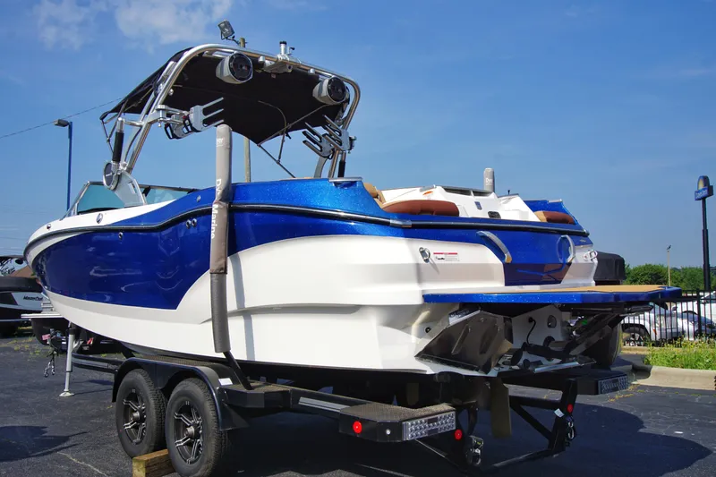 Slide: The Image of 2019 MasterCraft X24 boat on trailer, blue and white design, parked outdoors. - 1