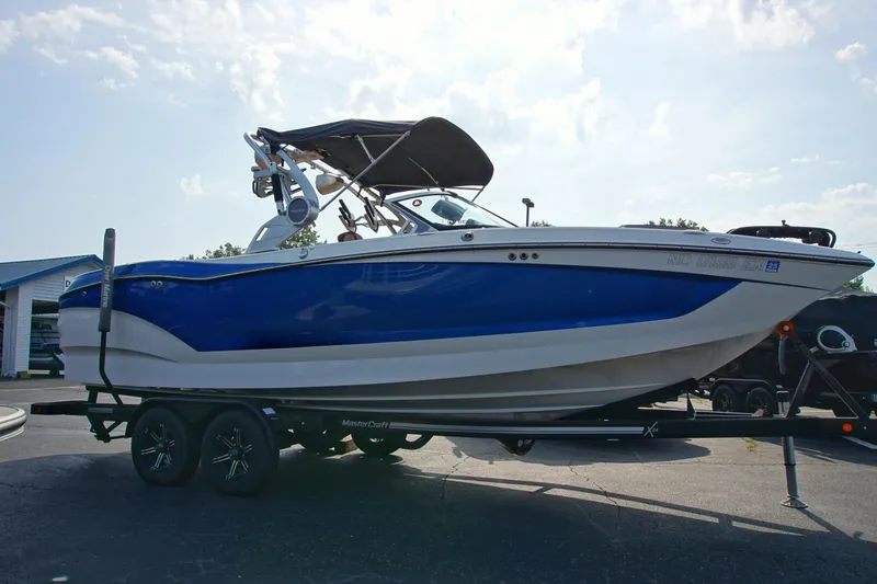 Slide: The Image of 2019 MasterCraft X24 boat on trailer, blue and white design, parked outdoors. - 4