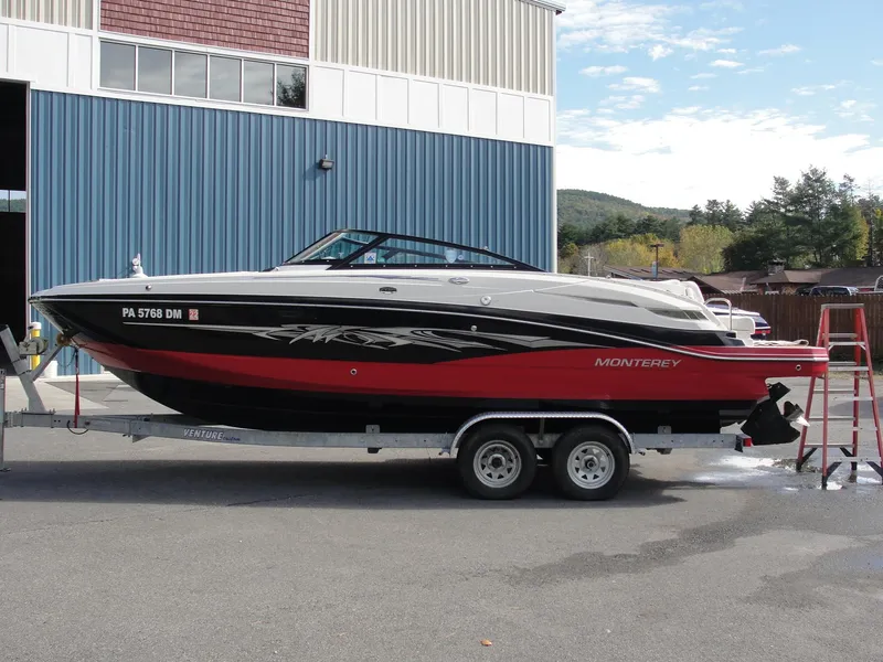 The Image of 2014 Monterey M5 boat on trailer, red and black design, parked outside a blue building. - 1