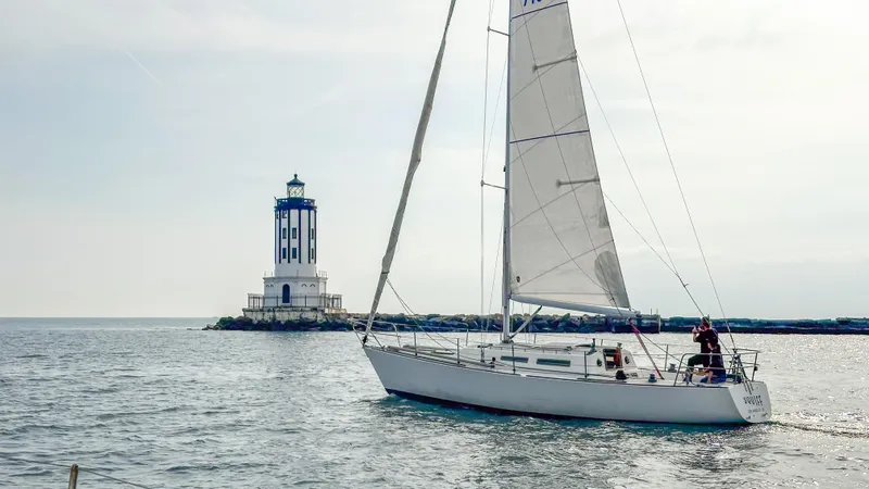 The Image of Sailboat Racing Sloop 1983 near lighthouse on calm sea. - 0