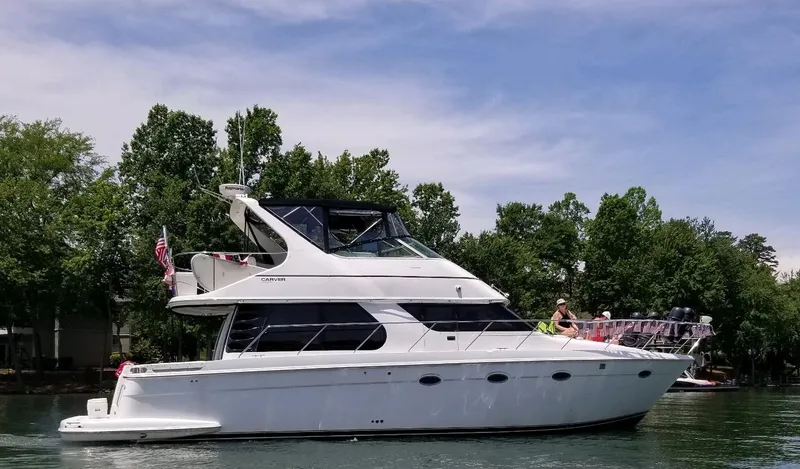 Slide: The Image of 2001 Carver 450 Voyager Pilothouse yacht on a serene lake with lush trees. - 1