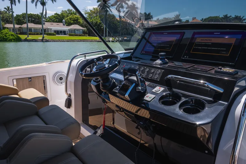 Slide: The Image of 2025 Pardo Yachts 38 helm with modern controls and dual screens, docked by waterfront homes. - 22
