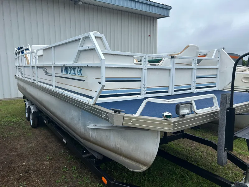 The Image of 1996 JC Suntoon 24 pontoon boat on trailer, parked near a metal building. - 0