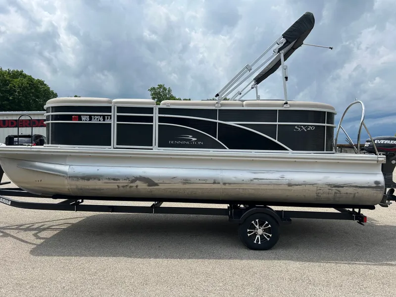 Slide: The Image of A 2019 Bennington 20SSRCX pontoon boat on a trailer, featuring a black Bimini top. - 3
