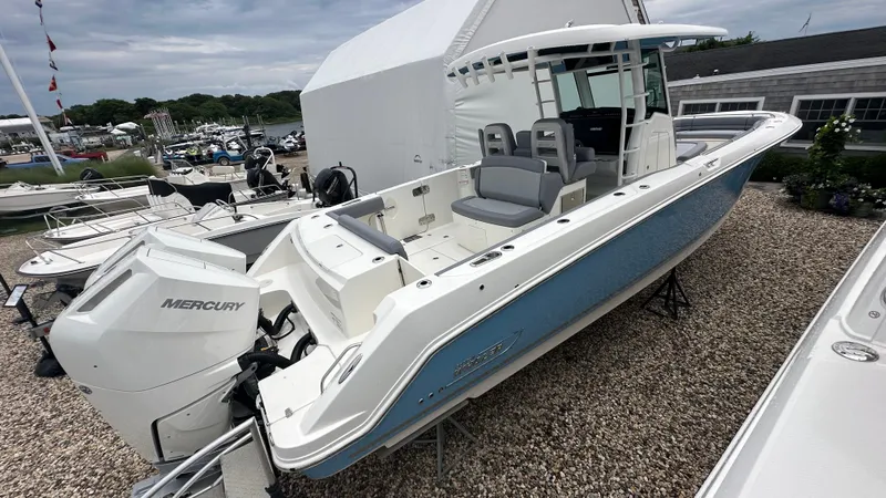 Slide: The Image of 2025 Boston Whaler 330 Outrage boat with Mercury engine, displayed outdoors on gravel. - 2