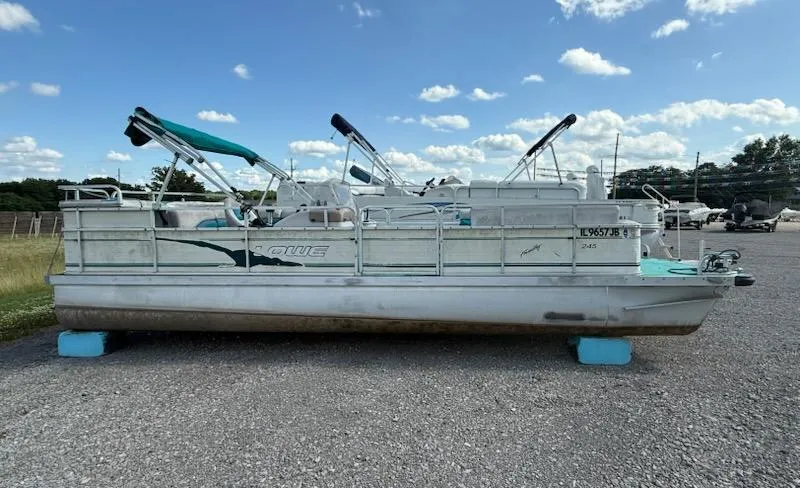 The Image of 1998 Lowe Family 245 pontoon boat on gravel, under a clear blue sky. - 1