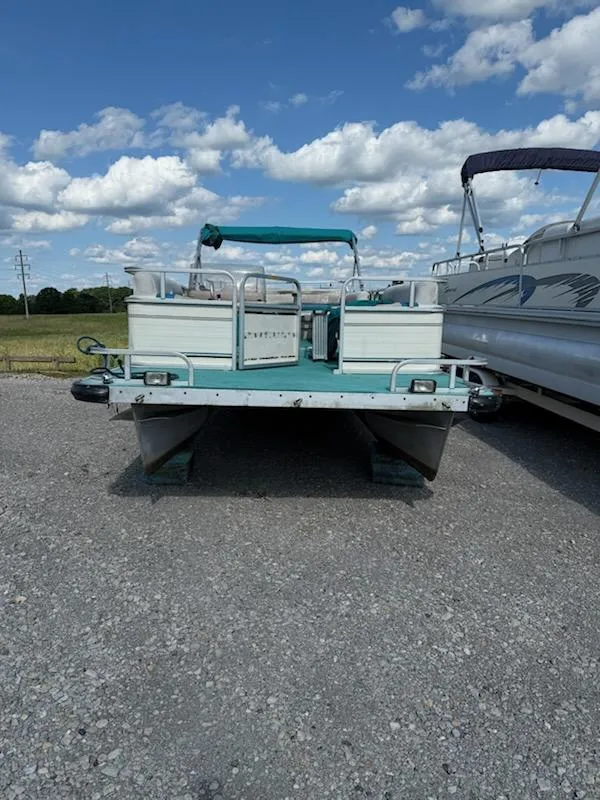 Slide: The Image of 1998 Lowe Family 245 pontoon boat on gravel under a blue sky. - 3