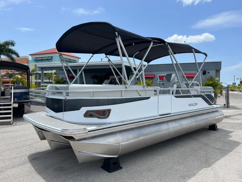 The Image of 2025 Avalon 2385 Venture 85 Quad Lounger Tri Toon boat with canopy, parked outdoors. - 1