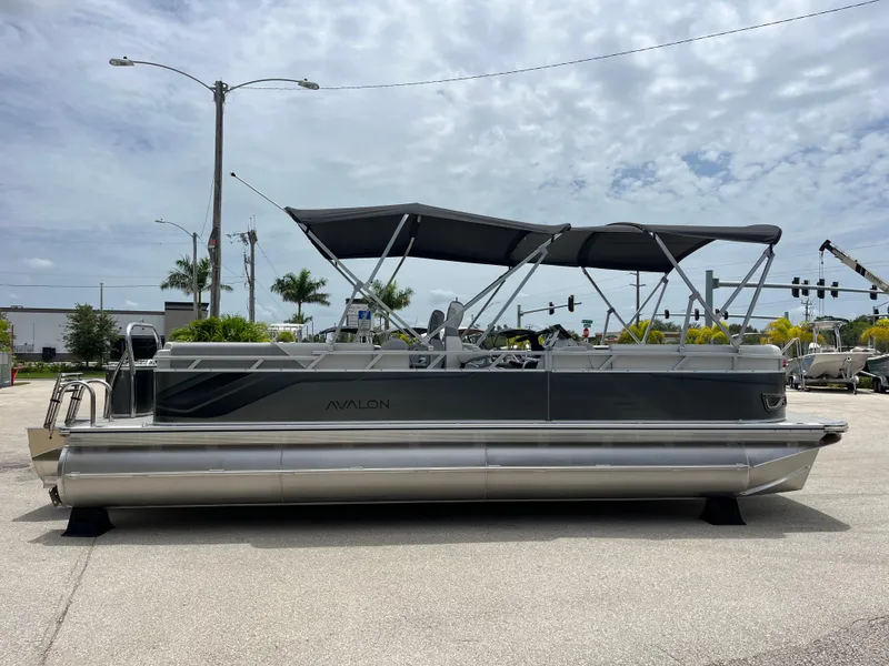 Slide: The Image of 2025 Avalon 2385 Venture 85 Quad Lounger Tri Toon boat, parked outdoors under cloudy sky. - 4
