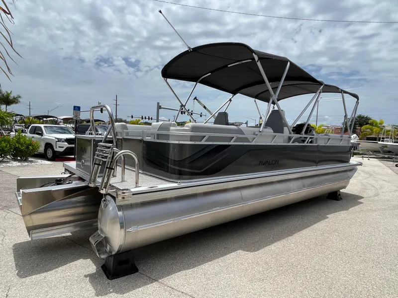 Slide: The Image of 2025 Avalon 2385 Venture 85 Quad Lounger Tri Toon boat with canopy, parked outdoors. - 5