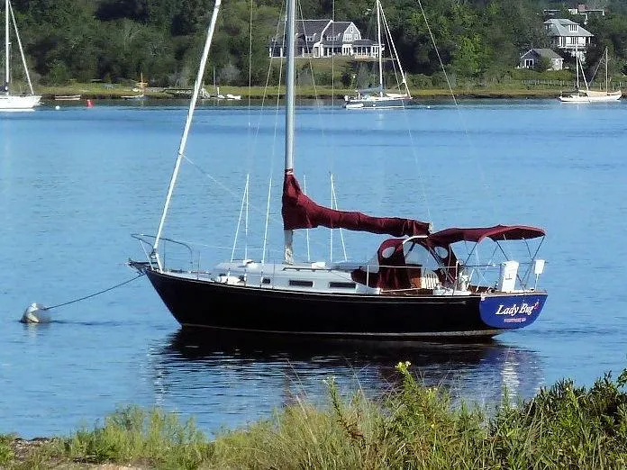 Slide: The Image of 1976 Bristol 34 sailboat anchored on a serene lake with lush greenery. - 11
