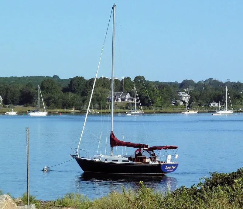 Slide: The Image of 1976 Bristol 34 sailboat moored on a serene lake with houses in the background. - 12