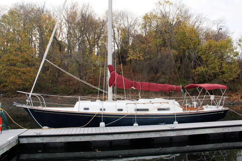 Slide: The Image of 1976 Bristol 34 sailboat docked by autumn trees, featuring a red sail cover. - 13