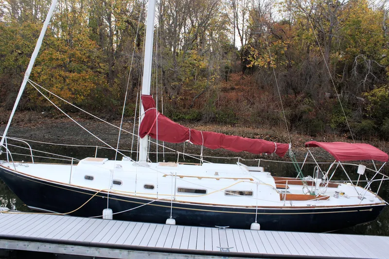 Slide: The Image of 1976 Bristol 34 sailboat docked, featuring red sail covers and autumn trees in the background. - 14