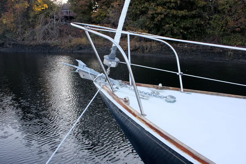 Slide: The Image of 1976 Bristol 34 sailboat bow with anchor, moored on calm water, surrounded by autumn trees. - 17