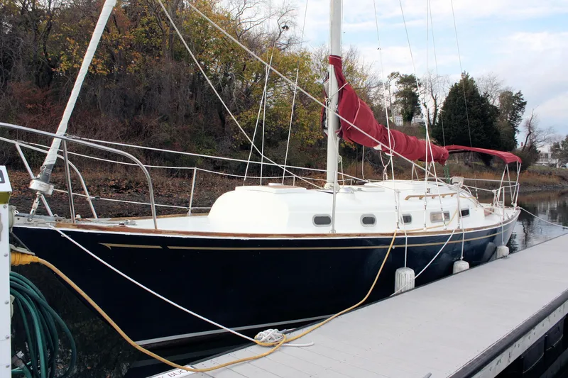 Slide: The Image of 1976 Bristol 34 sailboat docked, featuring a dark hull and red sail cover. - 19