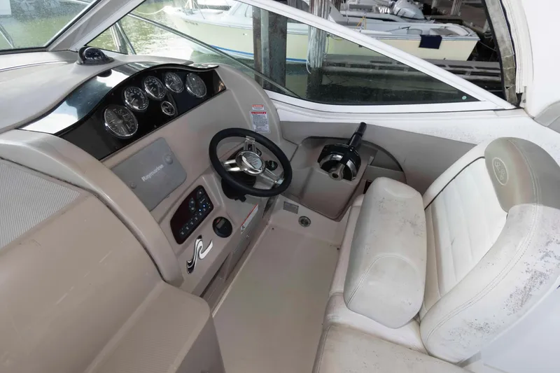 Slide: The Image of 2006 Sea Ray 290 Sundancer helm with steering wheel and gauges, featuring beige seating. - 2