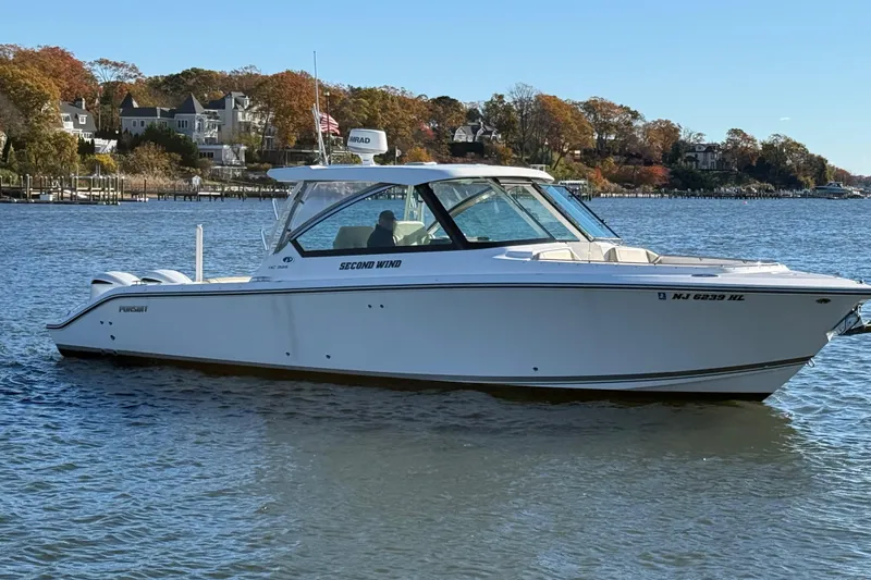 Slide: The Image of 2017 Pursuit DC 325 Dual Console boat on calm water, with scenic shoreline background. - 1
