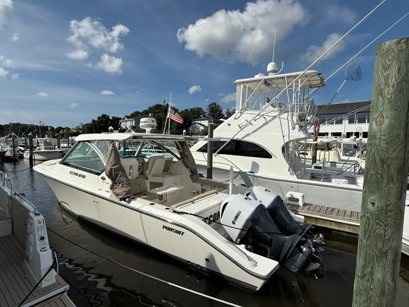 Slide: The Image of 2017 Pursuit DC 325 Dual Console boat docked at marina, sunny day, American flag visible. - 8