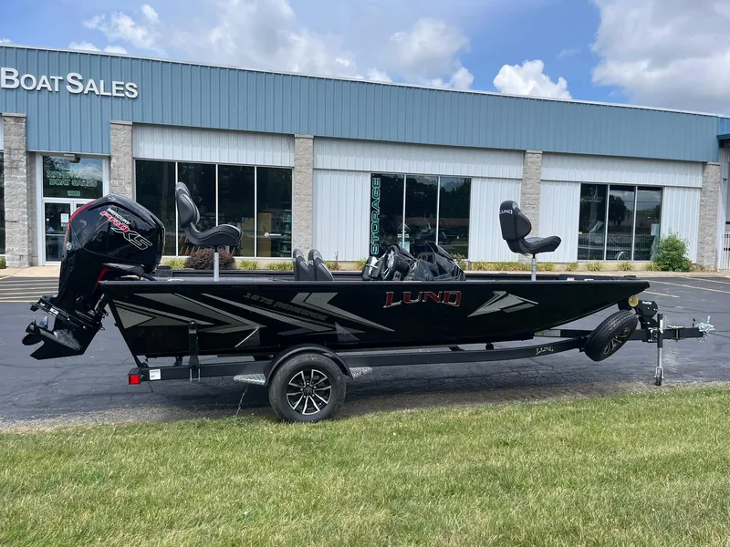 Slide: The Image of 2026 Lund 1875 Renegade SS boat displayed outside dealership, featuring sleek black design. - 1