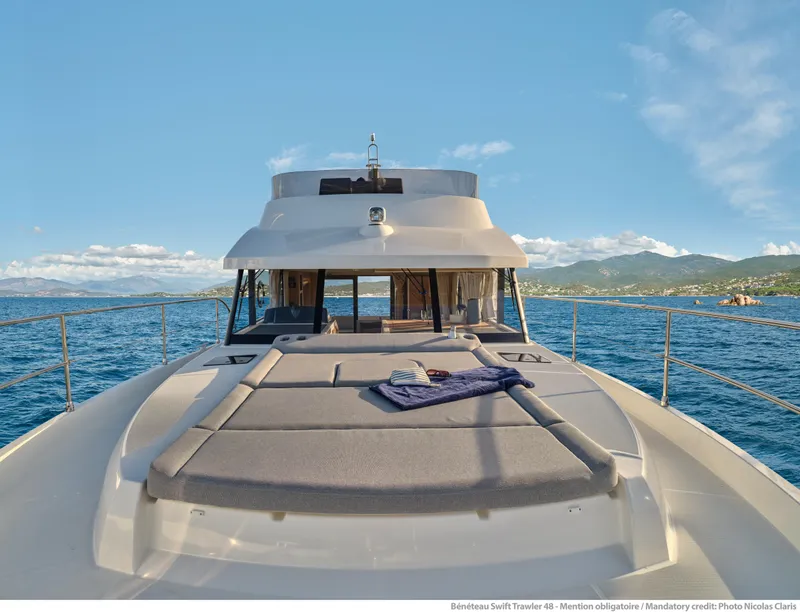 Slide: The Image of 2026 Beneteau Swift Trawler 48 cruising on open sea with scenic coastal backdrop. - 5