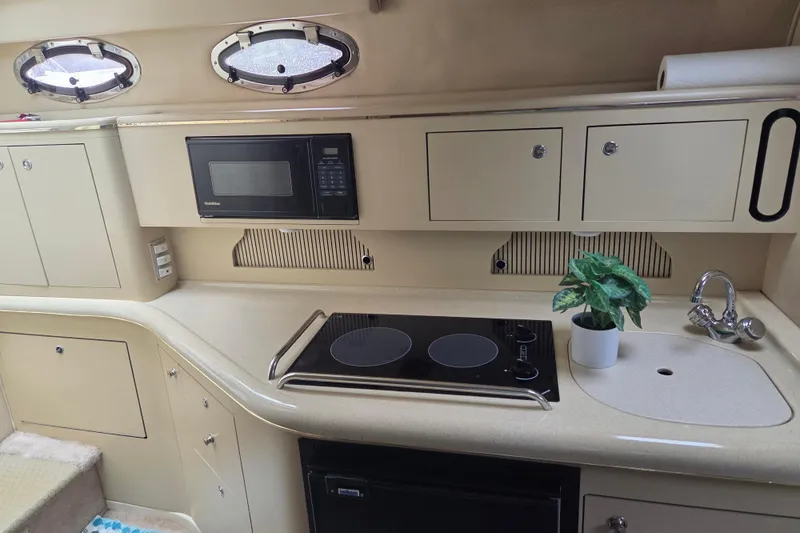 Slide: The Image of 1998 Sea Ray 310 Sundancer galley with stove, microwave, sink, and portholes. - 10