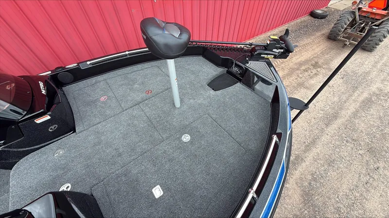 Slide: The Image of 2025 Nitro ZV19 boat deck with seating and trolling motor, parked near a red wall. - 3