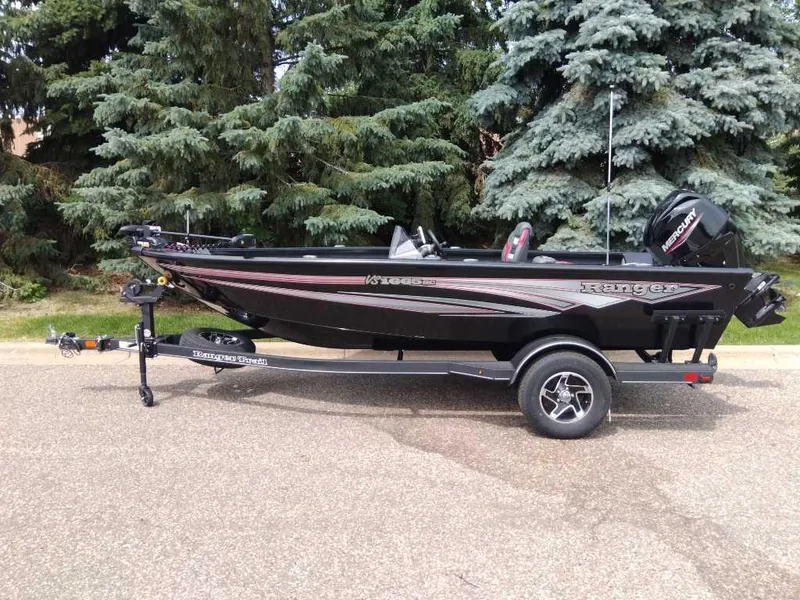 The Image of 2025 Ranger VS1665SC boat on trailer, parked near lush green trees. - 0