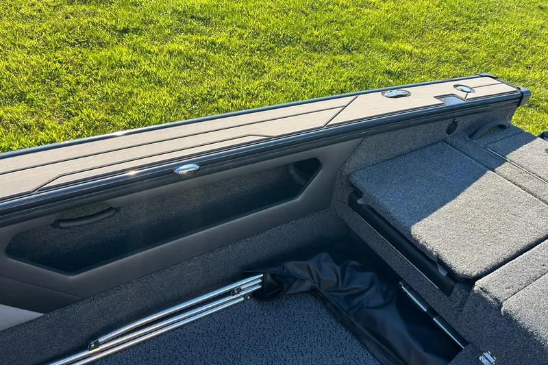 Slide: The Image of 2026 Lund 1875 Crossover XS boat interior with storage compartments and seating on grassy background. - 29