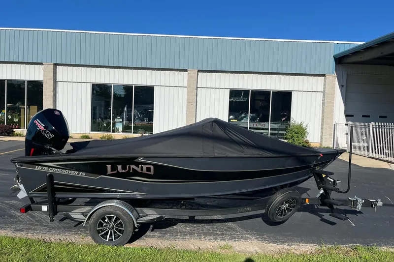 Slide: The Image of 2026 Lund 1875 Crossover XS boat with cover, parked outside a building. - 42