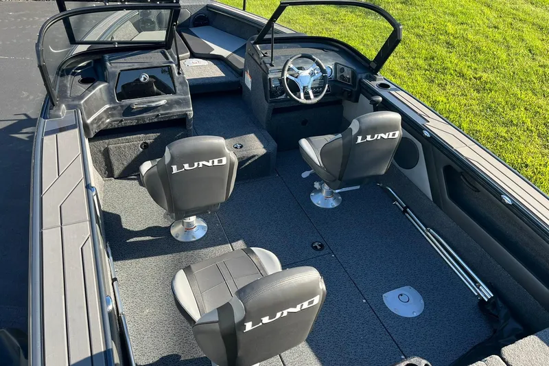 Slide: The Image of 2026 Lund 1875 Crossover XS boat interior with seating and steering wheel, on grass background. - 8