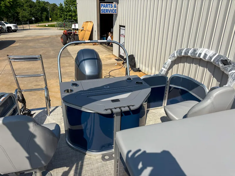 Slide: The Image of 2022 Trifecta CS 24RFC pontoon boat interior with seating and control panel, parked outside service area. - 4