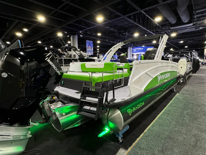 Slide: The Image of 2025 Paradigm 25SS pontoon boat with green accents and Mercury engine at indoor exhibition. - 6
