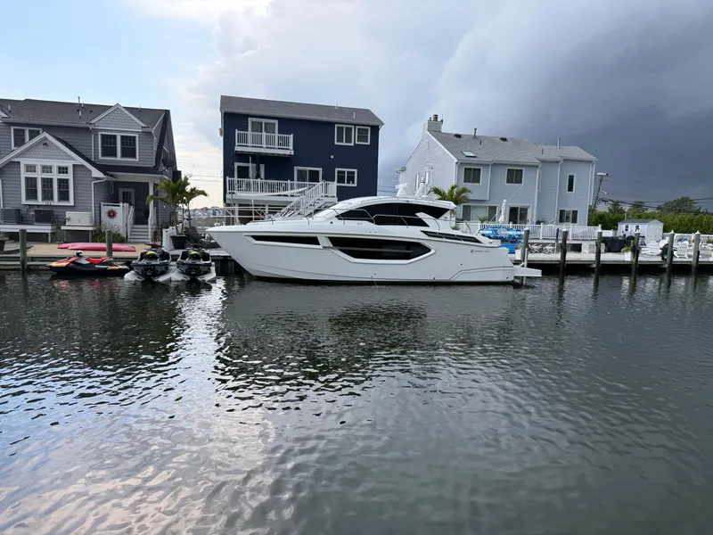 Slide: The Image of 2018 Cruisers Yachts 42 Cantius docked near waterfront homes under cloudy sky. - 4