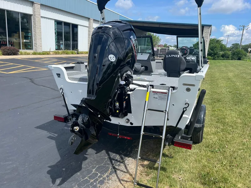 Slide: The Image of 2026 Lund 1675 Adventure Sport boat with Mercury outboard motor and ladder, parked outdoors. - 2