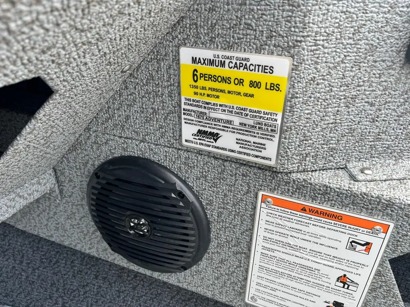 Slide: The Image of 2026 Lund 1675 Adventure Sport capacity label and warning stickers on textured surface. - 25