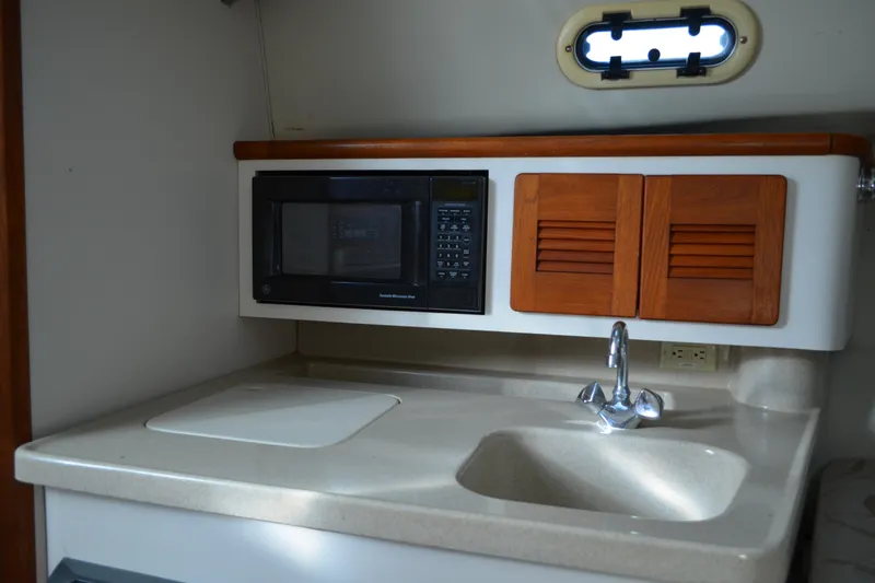 Slide: The Image of 2003 Pursuit 3000 Express boat kitchen with sink, microwave, and wooden cabinets. - 41