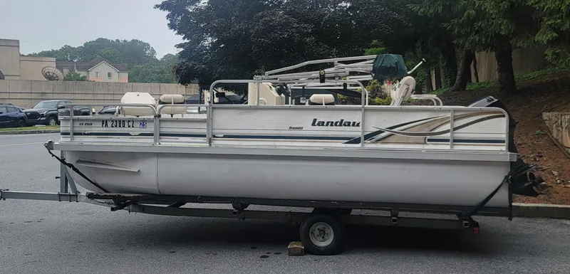 Slide: The Image of 1999 Landau 18 FISH pontoon boat on trailer, parked outdoors. - 0