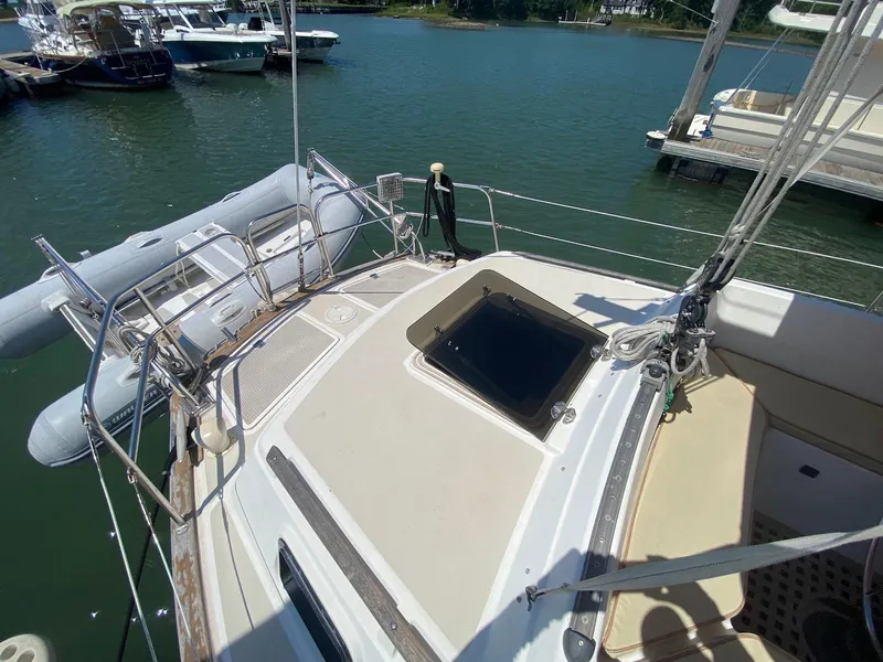 Slide: The Image of 1986 S2 11 Center Cockpit sailboat docked, featuring a spacious deck and nearby dinghy. - 10