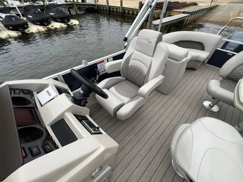Slide: The Image of 2018 Bennington SX 23 boat interior with plush seating and modern dashboard near docked jet skis. - 6